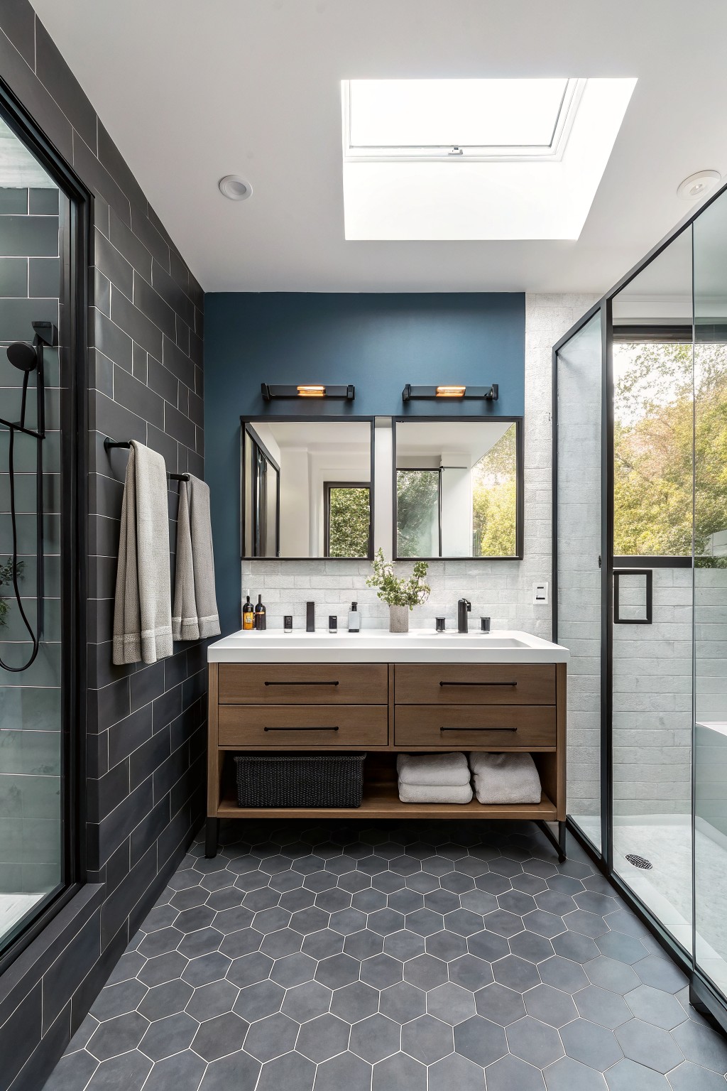 Modern bathroom with double wooden vanity, blue accent wall, skylight, and gray hex tiles