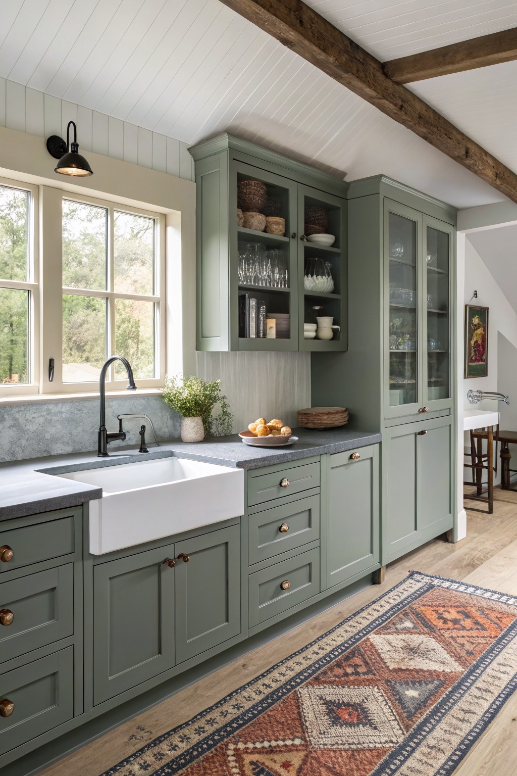 Sage green kitchen cabinets with a white farmhouse sink and dark countertops.