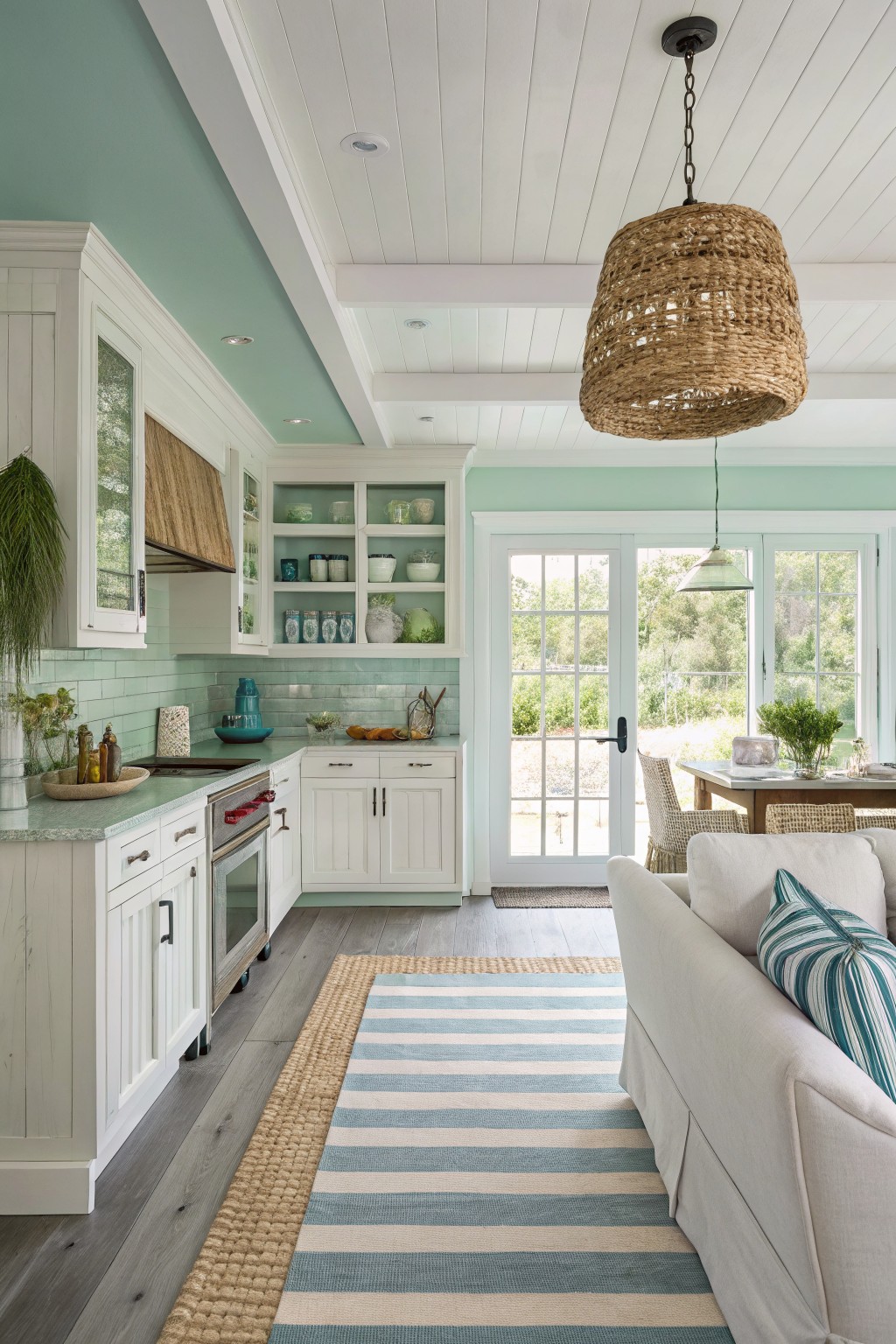 Bright coastal kitchen with white cabinets, mint accents, woven light, and striped rug.