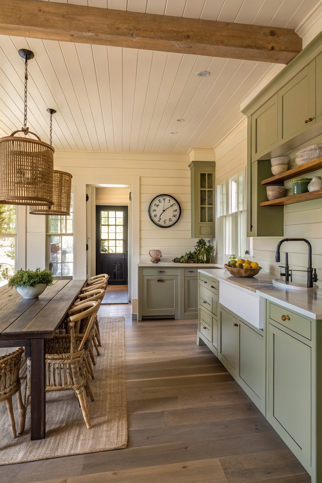Sage green kitchen cabinets in an open dining space with wood floors.
