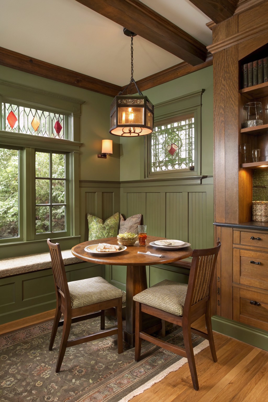 Sage green walls in a wood-trimmed dining nook with a round table.