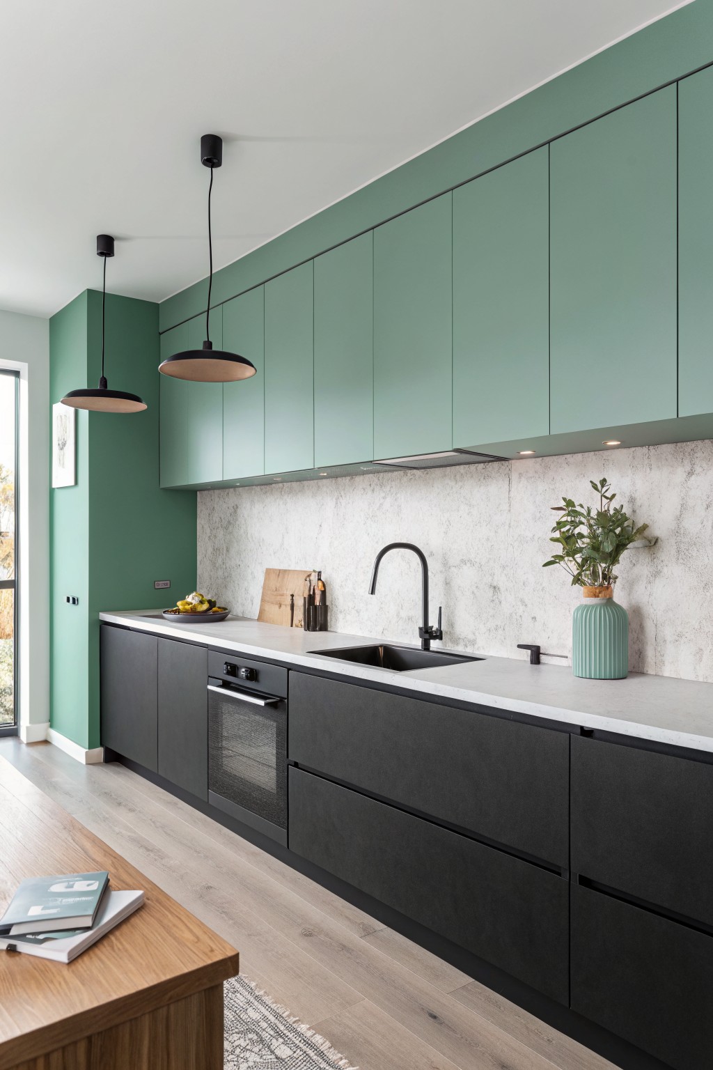 A kitchen with soft sage green upper cabinets above dark lower cabinets.