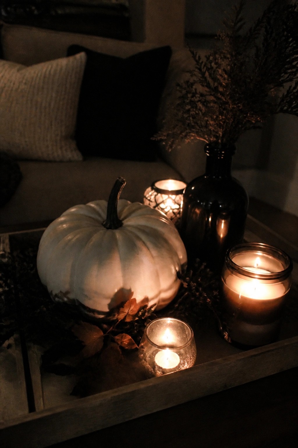 White pumpkin with lit candles, dried plants, and autumn leaves on wooden tray
