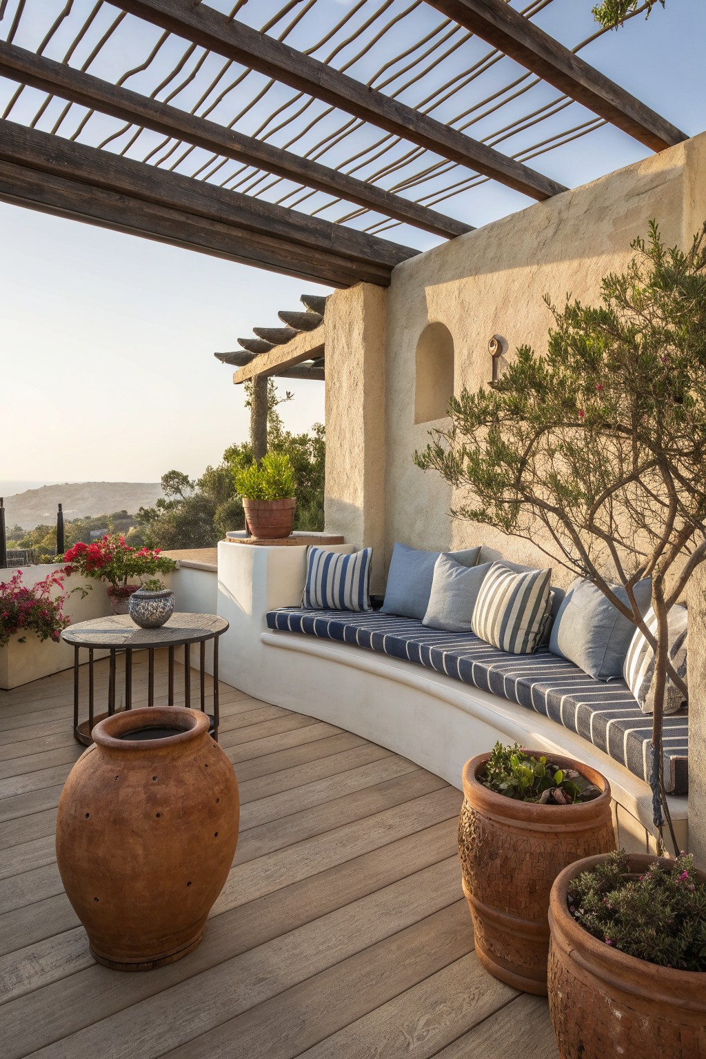 Mediterranean patio with curved bench, blue striped cushions, terracotta pots and wooden pergola.