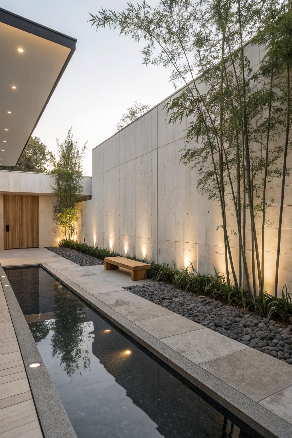 Modern courtyard with reflecting pool, bamboo grove, wooden bench, and lit concrete walls.