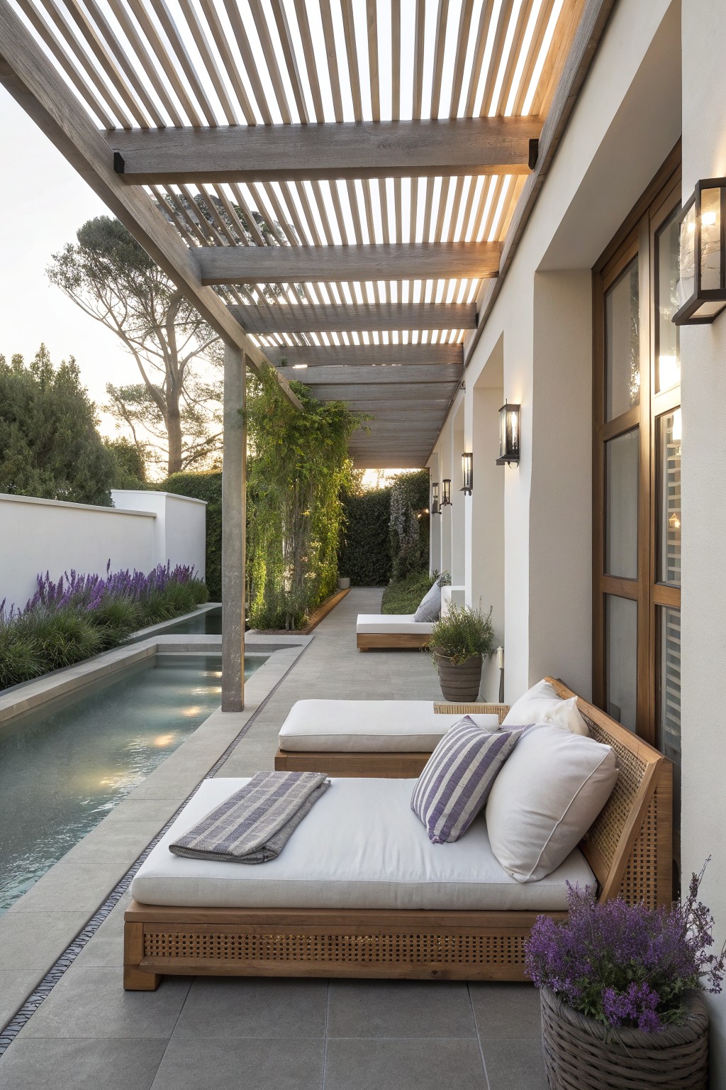 Wooden lounge chairs with cushions beside a pool under a slatted pergola