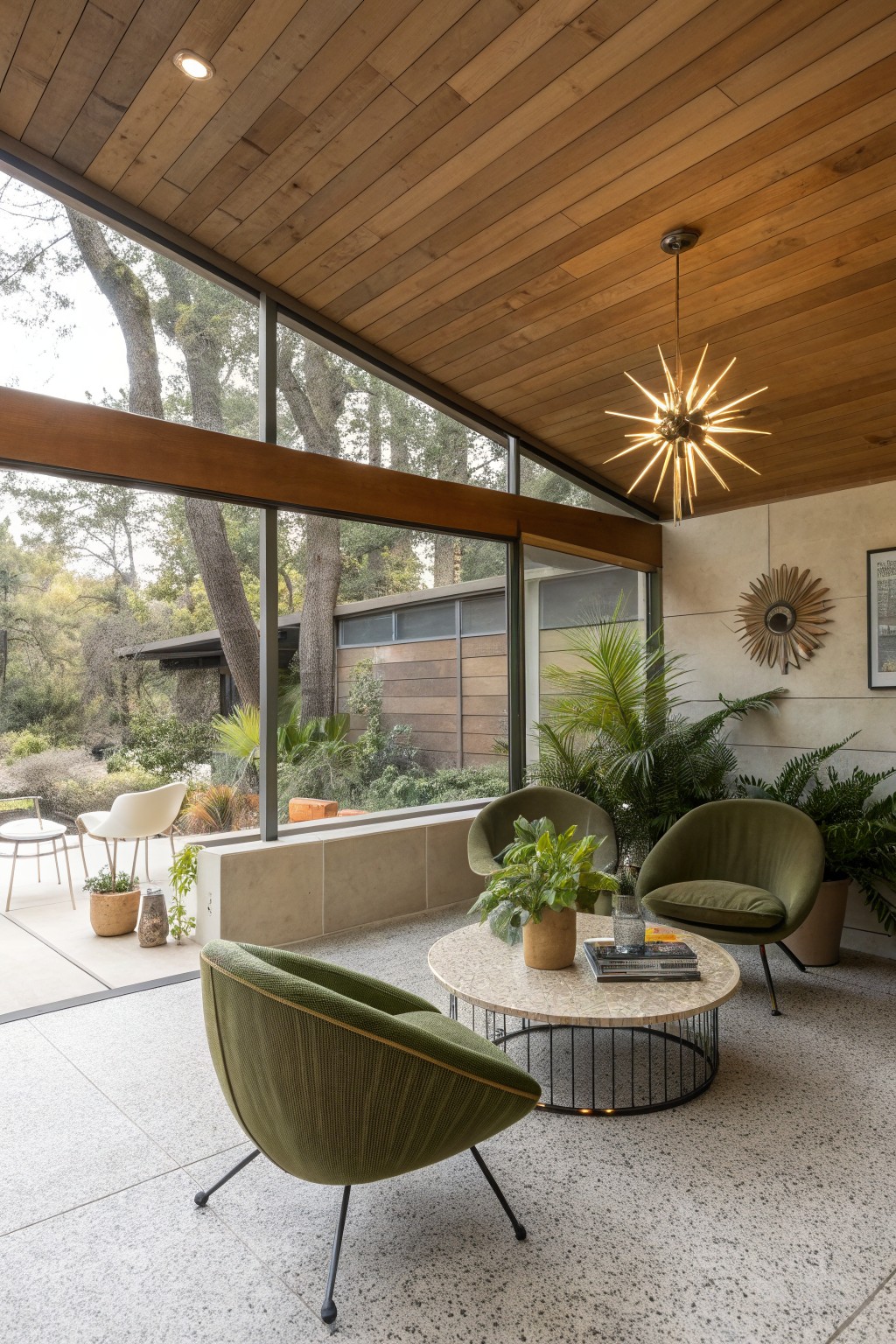 A covered patio shows three green upholstered lounge chairs arranged around a round coffee table beneath a wood ceiling.