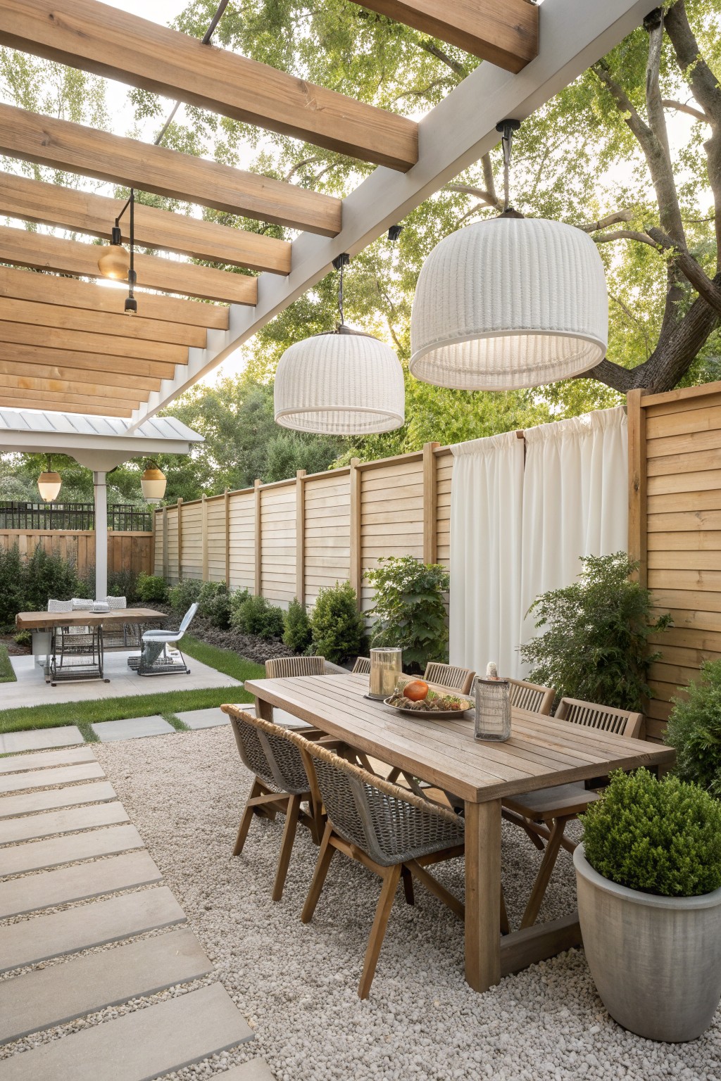 Wooden patio table with woven chairs under large white pendant lights on gravel