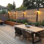 A wooden deck dining area with a long horizontal wood slat privacy fence behind the table and chairs.